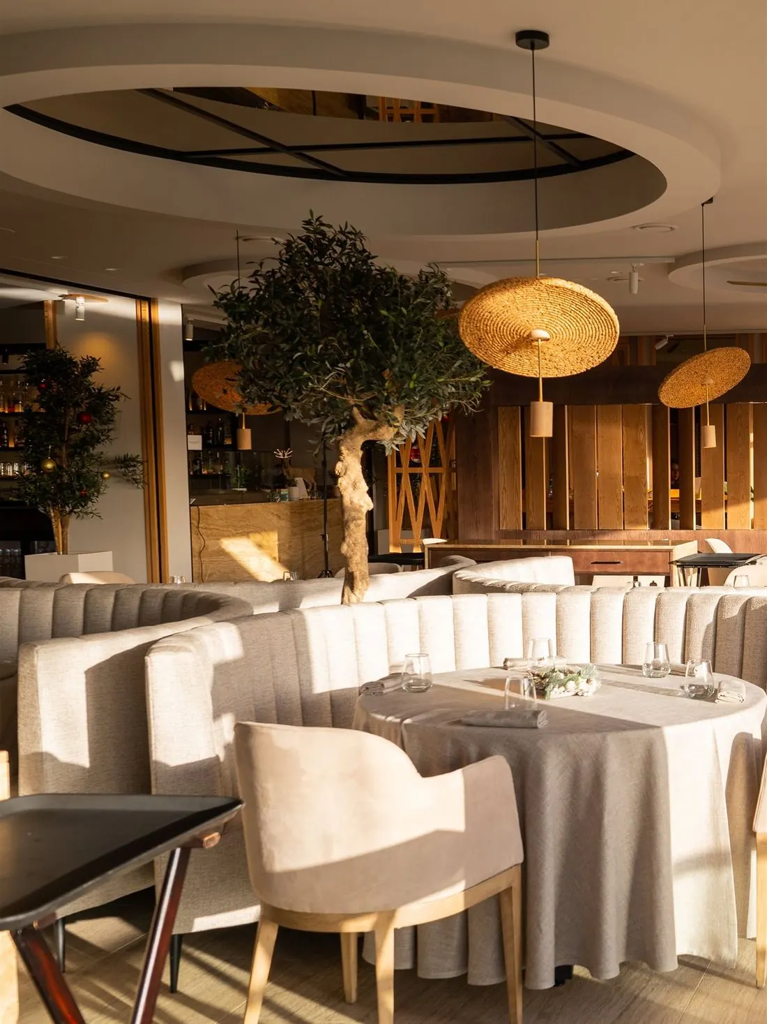 Sala luminosa con un olivo, lámparas de fibra y sofás tapizados en tono crudo