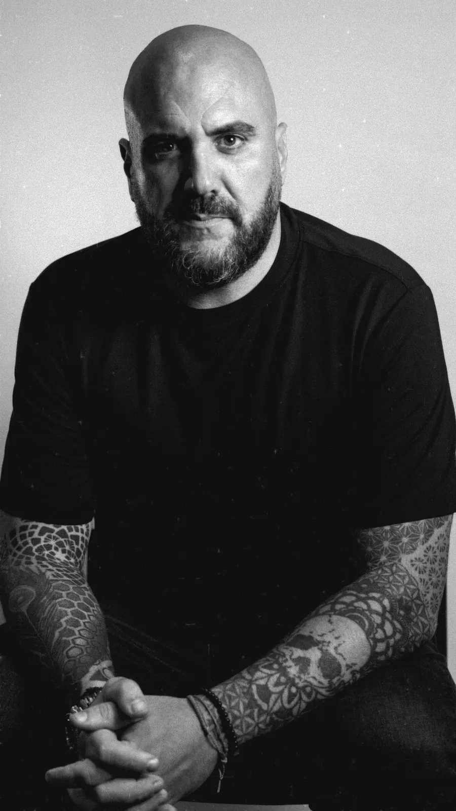 Retrato en blanco y negro de Juanra Calavera, sentado, con camiseta oscura y las manos entrelazadas