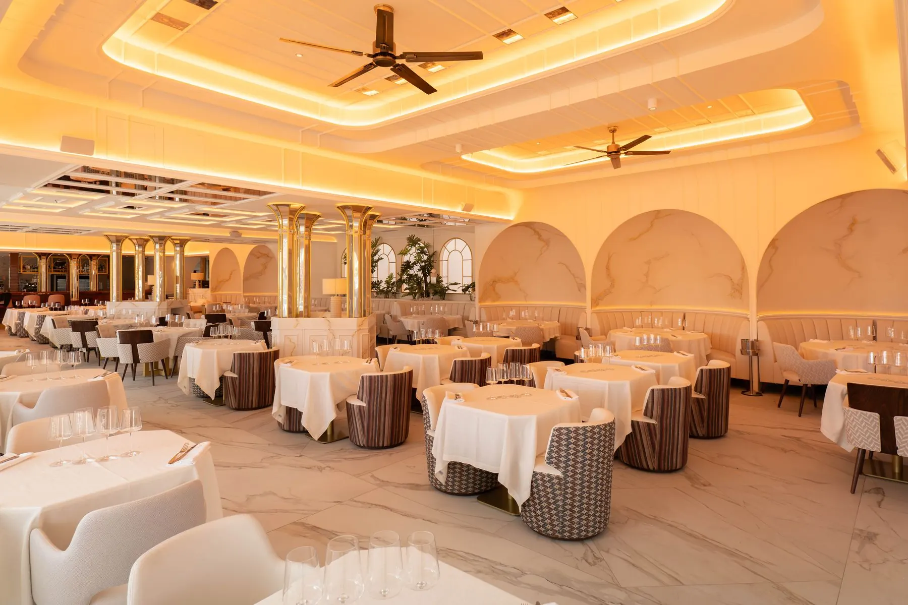 Sala de restaurante con arcos de mármol, columnas doradas y mesas con mantel blanco